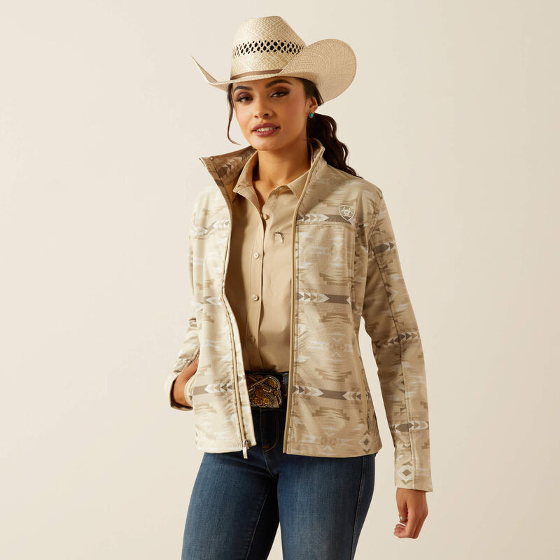 Woman wearing a beige patterned jacket, beige shirt, blue jeans, and a cowboy hat on a beige background