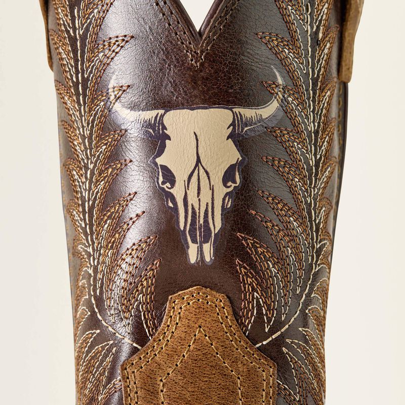 Close-up of a brown leather western boot shaft featuring a stitched steer skull design, embroidered leaf patterns, and a tan pull tab on a light beige background.
