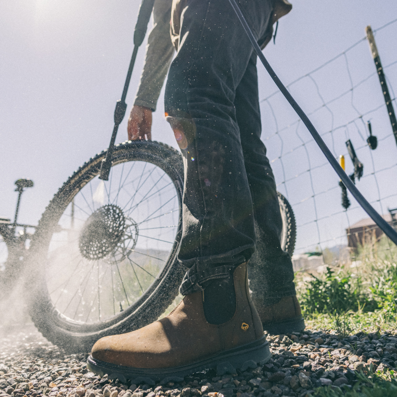 Person wearing brown boots with a tire on a gravel surface