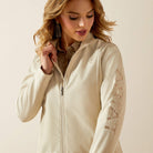 Woman wearing a beige jacket with 'Ariat' branding on a plain background