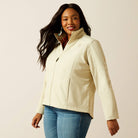 Woman wearing a cream jacket and blue jeans on a beige background