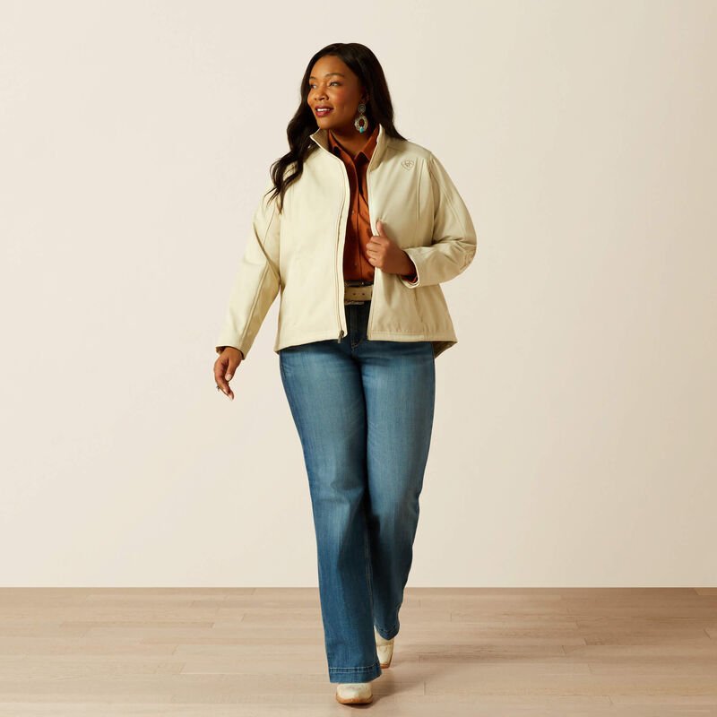 Woman wearing a beige jacket and blue jeans against a plain background