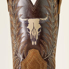 Close-up of a brown leather western boot shaft featuring a stitched steer skull design, embroidered leaf patterns, and a tan pull tab on a light beige background.