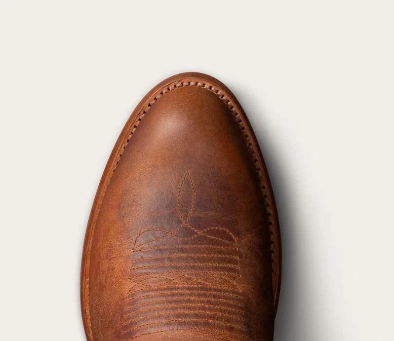 Top-down close-up of a brown leather boot toe showing the vamp, stitching, and a subtle western-style stitched motif on a light off-white background.
