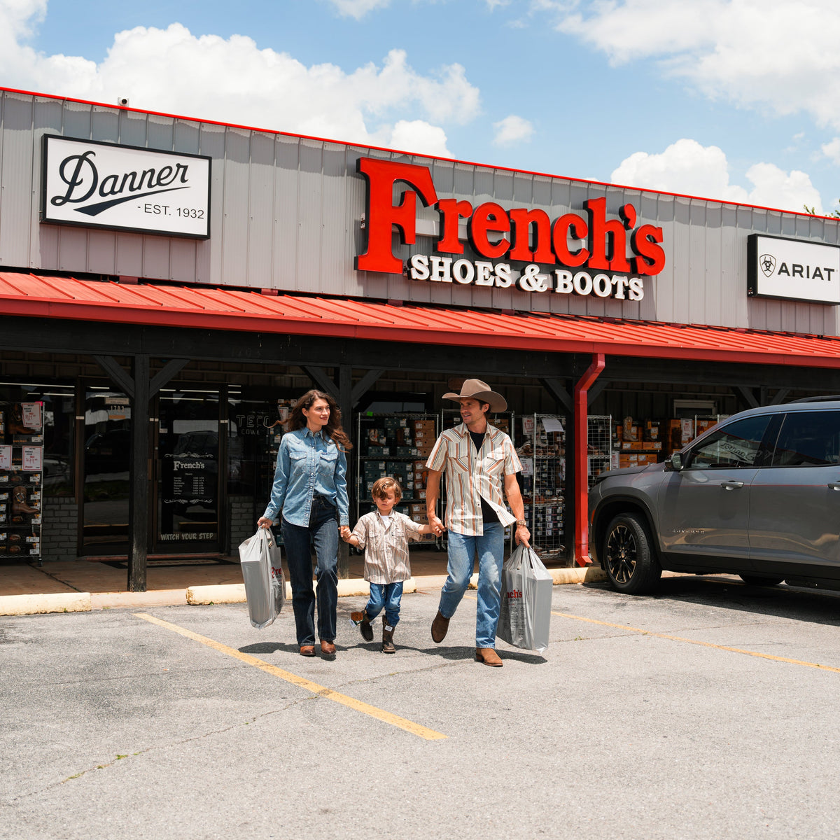 A family of three walks out of a retail store parking lot carrying shopping bags. The storefront has a large red 'French's Shoes & Boots' sign, with other visible brands including Keeen, Danner, and Ariat.