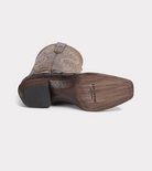 Brown cowboy boot with detailed sole on a light gray background