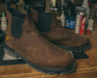 Brown leather boots on a wooden workbench with tools and supplies in the background