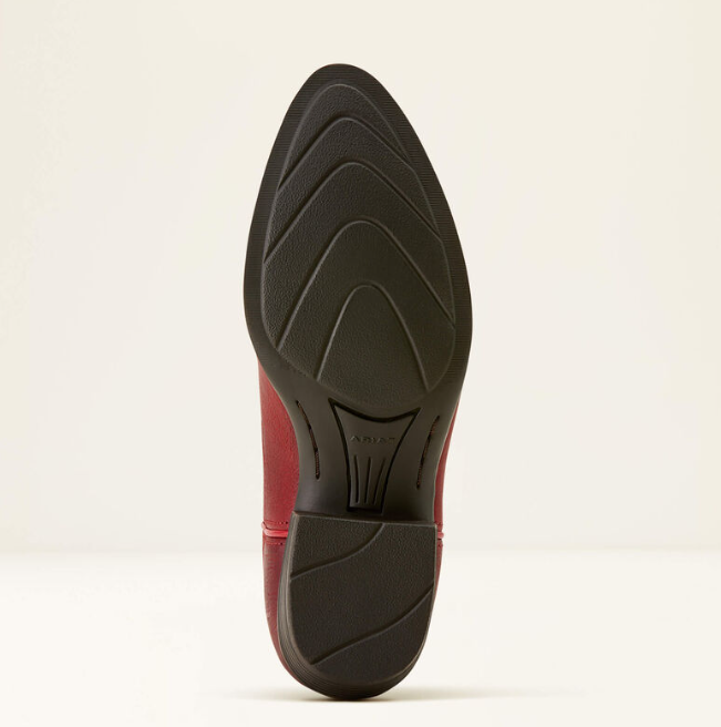 The pointed toe and textured black outsole of a red and black boot, shown from a top-down view against a light cream background.
