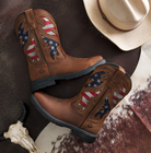 Brown cowboy boots with American flag design on a rustic surface with a hat and cow skull.