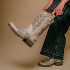 Person wearing white cowboy boots with intricate designs on a beige background
